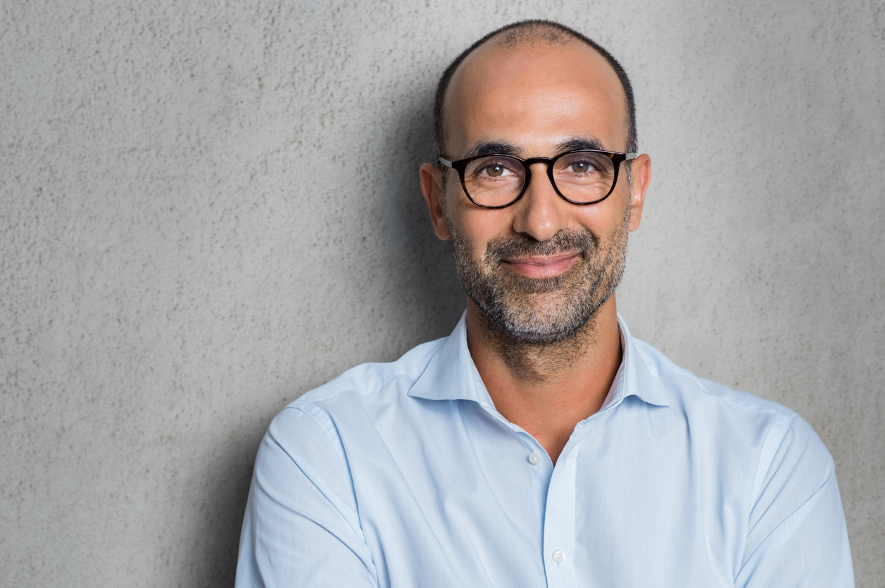 Portrait of a mature businessman wearing glasses on grey background. Happy senior latin man looking at camera isolated over grey wall with copy space. Close up face of happy successful business man.